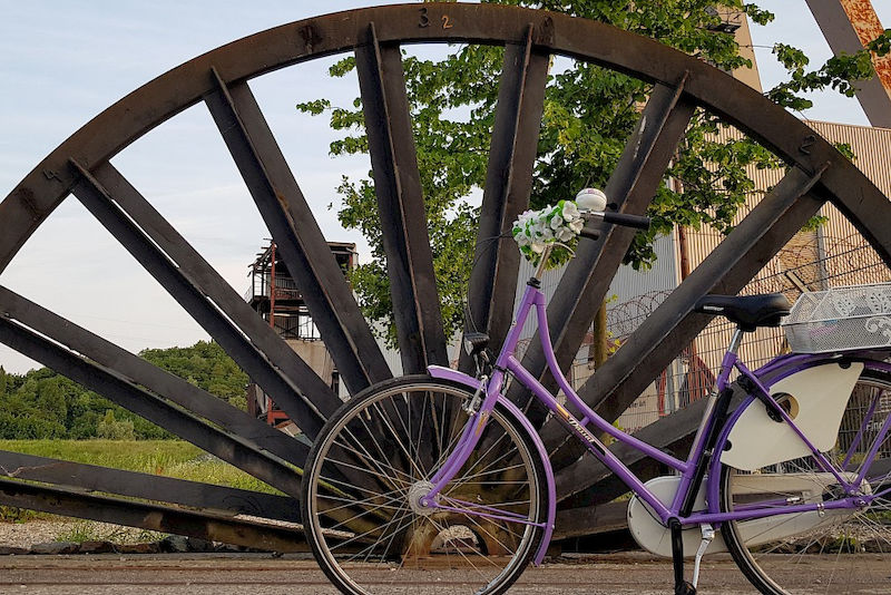 Lena aus Deutschland hat ihr violettes Fahrrad vor einem alten Förderrad fotografiert. Sie weist damit die Ähnlichkeit der beiden Kreise hinsichtlich ihrer Sektoren hin und ist Drittplatzierte im Fotowettbewerb.