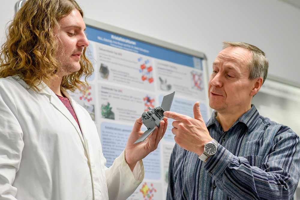 Nils Kotschote (li.) und Stefan Ebbinghaus schauen sich das Modell einer Raumsonde an. Sie forschen in einem Projekt, das die Ionenantriebe von Sonden, Satelliten und Co. sicherer und preiswerter machen soll.