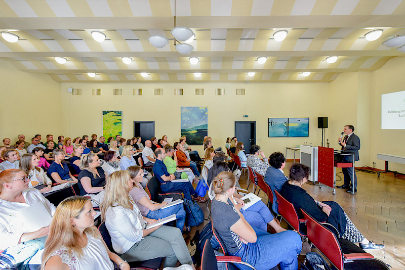 Minister Jan Riedel stand in einem gut gefüllten Hallischen Saal: Die Zahl der Seiteneinsteigerinnen und Seiteneinsteiger hat sich in diesem Jahr verdoppelt.